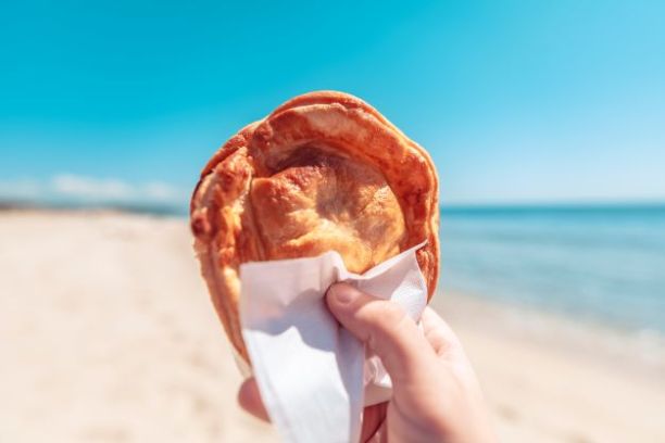 a hand holding a donut in front of a beach