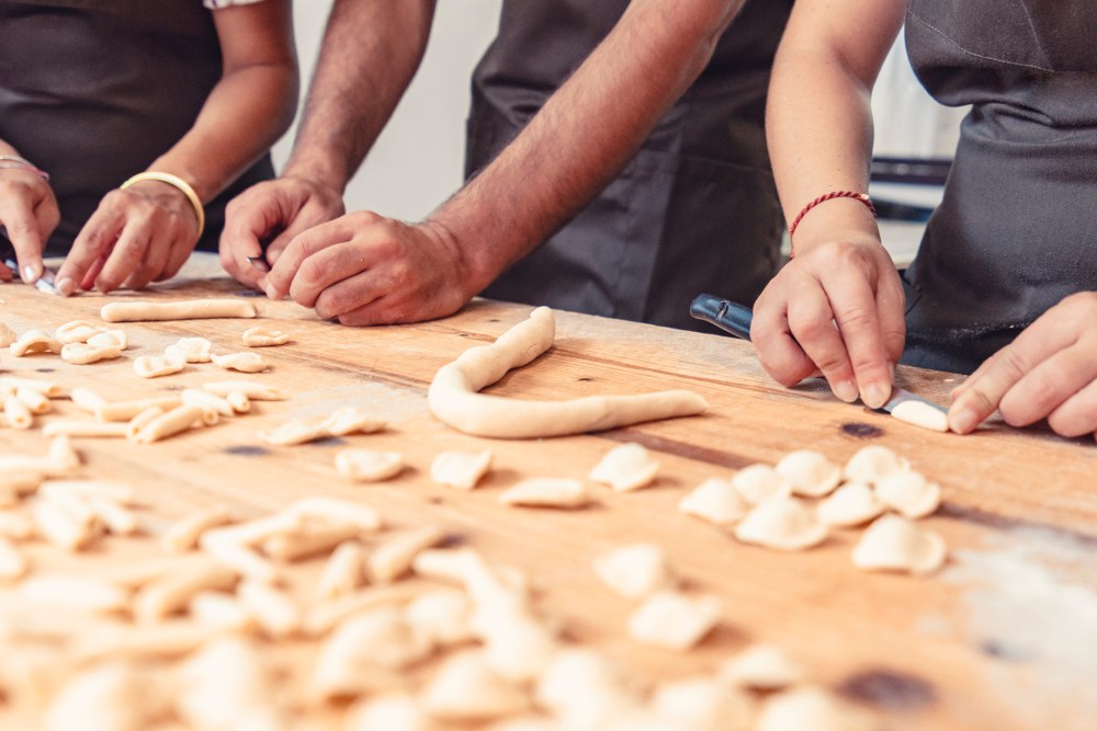 People shaping dough on a wooden table, preparing pasta with hands.