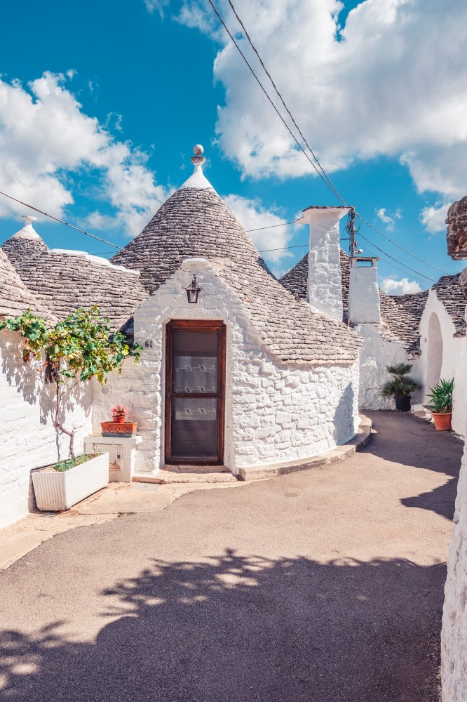 Trulli house with conical roof under blue sky with clouds.