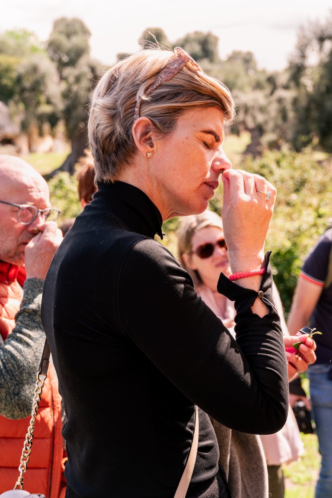 Woman smelling something outdoors with a group of people around her.