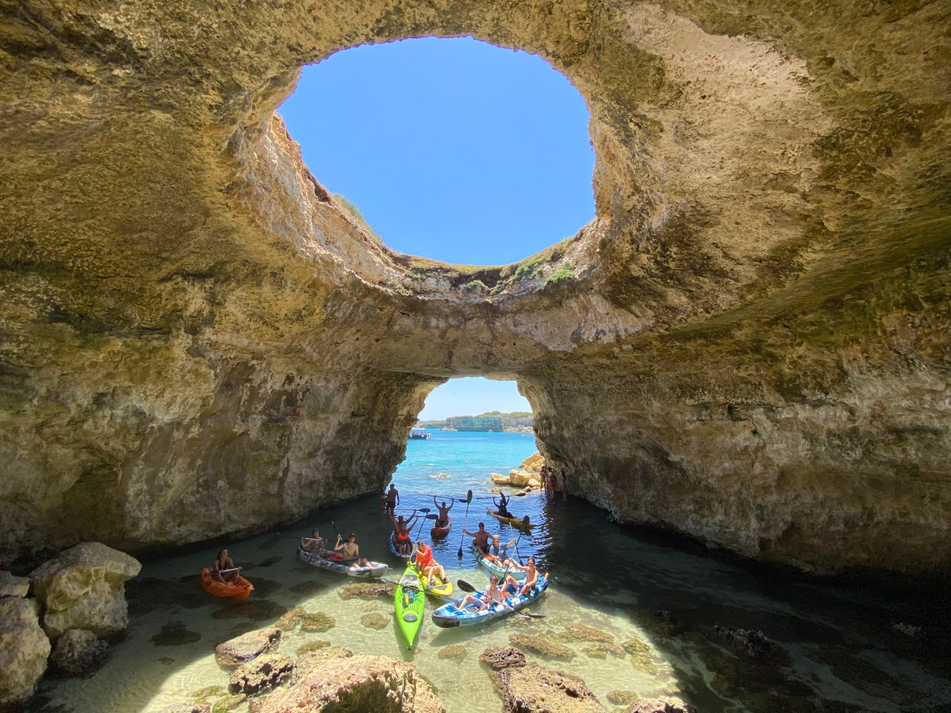Cave with circular openings and people kayaking in the water below.