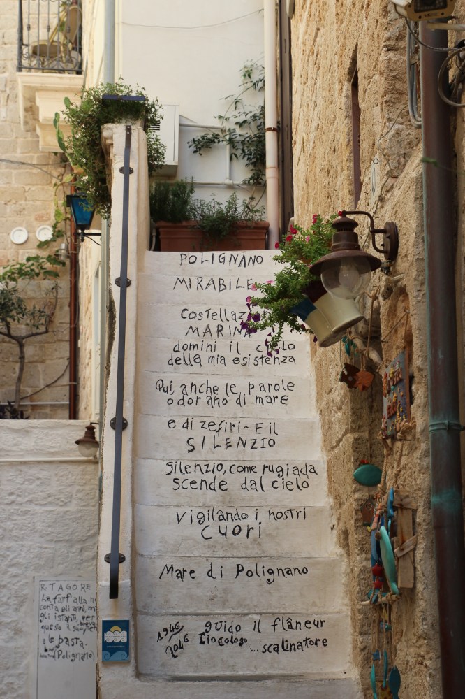 Stone steps with poetic text, plants, and a rustic lamp in a narrow alleyway.