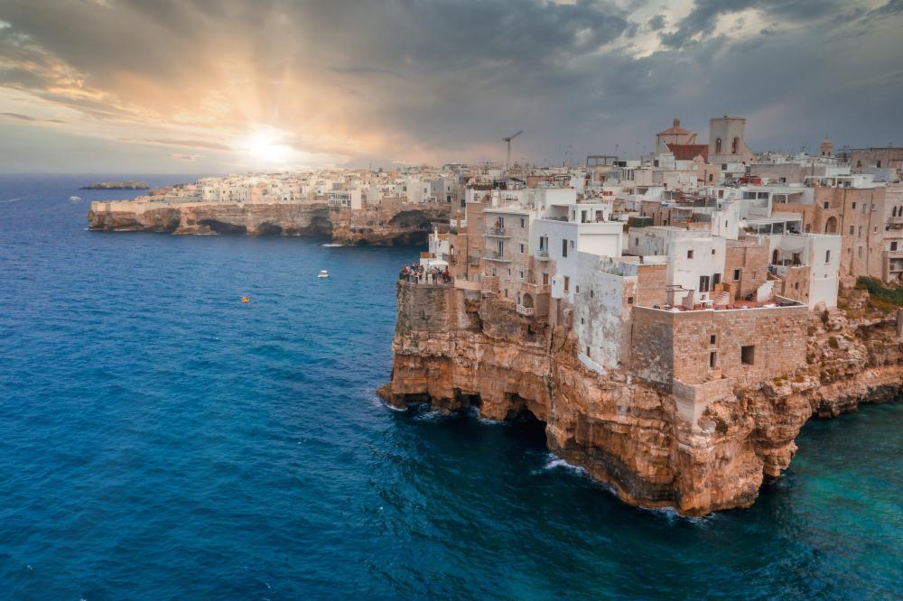 Coastal town with white buildings on cliffs at sunset overlooking the sea.